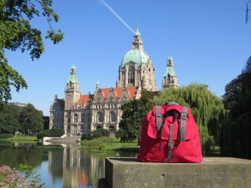 Ein roter Rucksack steht vor dem Maschteich auf einem Betonklotz; im Hintergrund des Neue Rathaus.